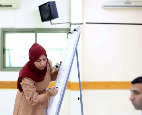 مدرّبة تشرح على اللوح الورقي خلال تدريب في المركز مدرّبة تكتب على اللوح الورقي خلال جلسة تدريبية في المركز الفلسطيني للديمقراطية وحل النزاعات